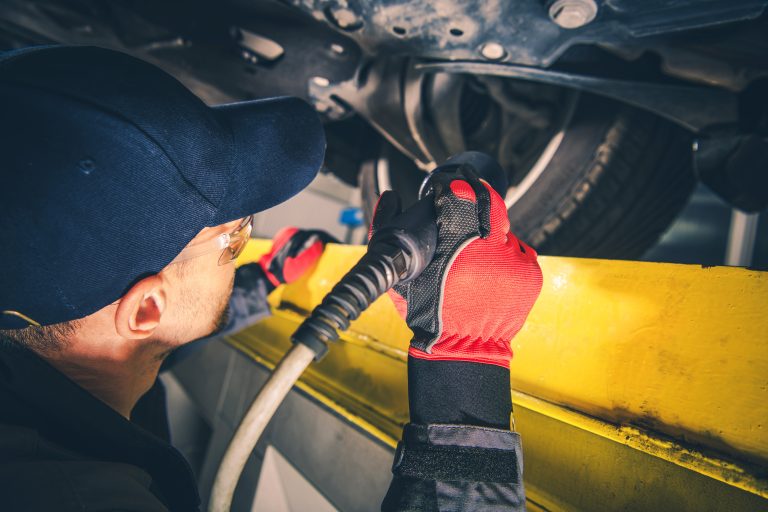 Professional Mechanic Checking Vehicle Undercarriage Using a Flashlight During Scheduled Car Inspection. Automobile Maintenance Theme.